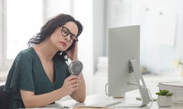 Woman managing hot flashes with a fan.  